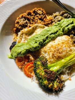 Fresh vegetarian brunch plate with sunny side up egg, roasted broccoli, carrots, and vegan crumbles in natural light.