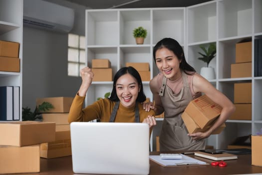 Two happy women celebrating success in warehouse with laptop.