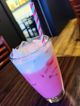 Refreshing Thai Pink Milk in a clear glass with striped straw, set in a cozy Fort Wayne cafe.
