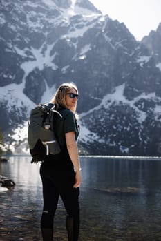A traveler girl with a backpack enjoys the stunning view of a mountain range and a lake, with snowcapped peaks in the background