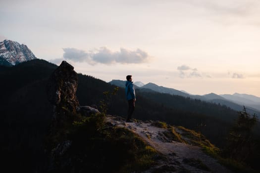 A person gazes at the mountain range from the summit, surrounded by vast natural landscapes of grasslands and clouds in the sky