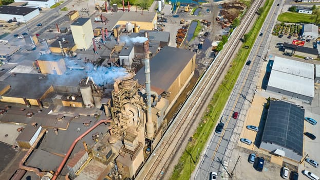 Aerial view of an active industrial complex in Warsaw, Indiana, showcasing smokestack emissions and robust connectivity.