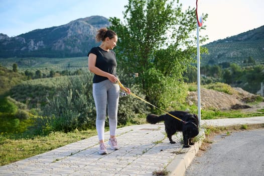 Full length portrait of happy woman in taking her dog for a walk on leash in the nature. Multi ethnic enjoying walk with her pedigree purebred black cocker spaniel dog in the mountains nature outdoors