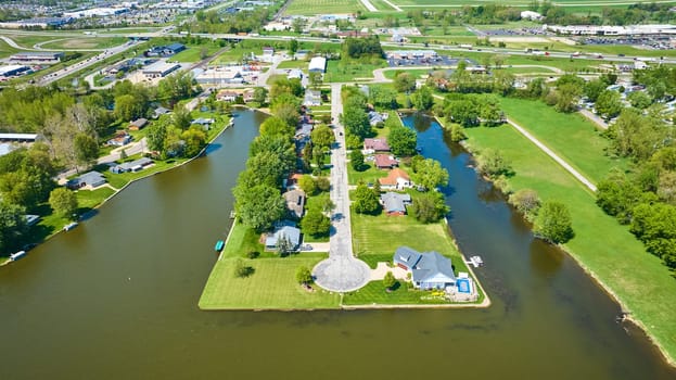 Aerial view of Warsaw, Indiana: serene waterway divides a lush suburban landscape with unique community park.