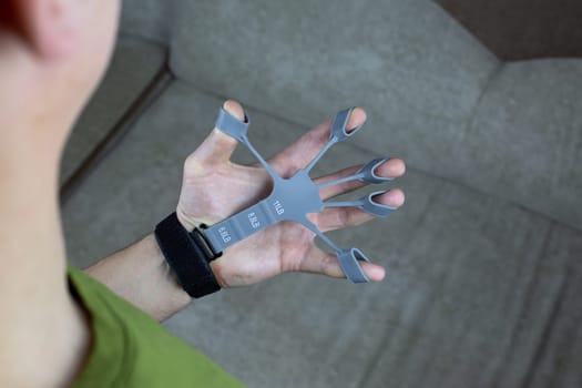 Man hand performs exercises with special finger trainer machine to develop arm strength and flexibility, spread fingers with silicone finger exerciser against joint disease