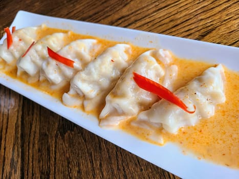 Elegant spicy Thai dumplings on a rustic table in Fort Wayne, served with a vibrant orange sauce.