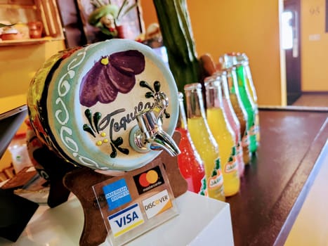 Hand-painted 'Tequila' dispenser in a cozy Fort Wayne cafe, with modern payment options and colorful drink bottles.