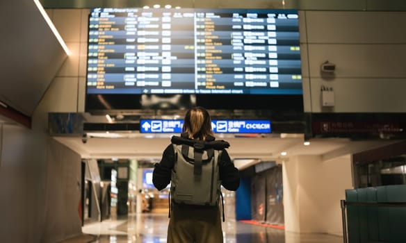 Young Asian woman in international airport looking at flight information board, checking her flight.