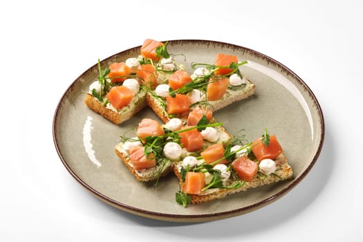 Appetizing bruschettas with salmon gravlax, mozzarella and cream cheese garnished with microgreen served on plate for breakfast. Fusion of Mediterranean and Nordic cuisines