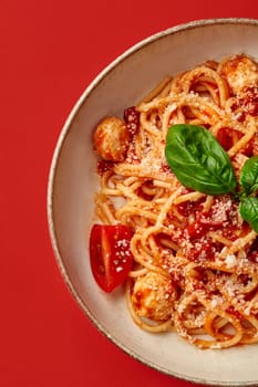 Closeup of rich Italian style arrabbiata pasta with spicy tomato sauce, meatballs and grated parmesan garnished with fresh aromatic basil, presented on vibrant red background