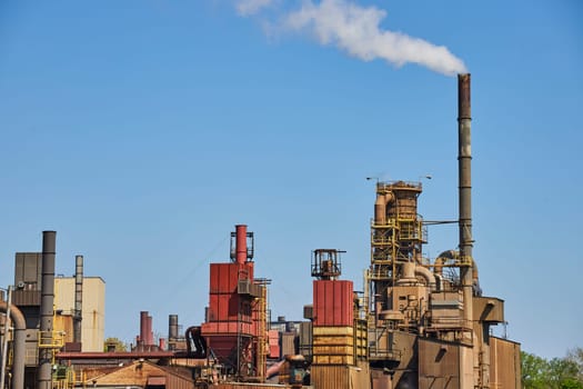 Industrial complex in Warsaw, Indiana with active smokestacks under a clear blue sky, symbolizing energy production and environmental impact.