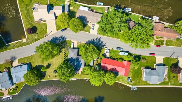 Aerial view of a vibrant Warsaw, Indiana neighborhood by a tree-lined lake, showcasing diverse homes and leisurely lifestyle.