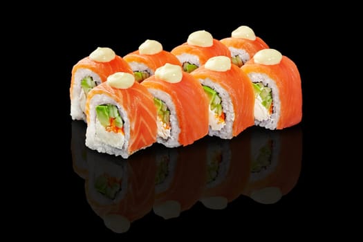 Classic Japanese sushi rolls filled with avocado, tobiko and cream cheese topped with fresh salmon slices and drops of mayo, presented on glossy reflective black background