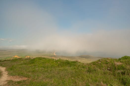 A foggy day with a cloudy sky and a grassy hill. The sky is blue and the clouds are white