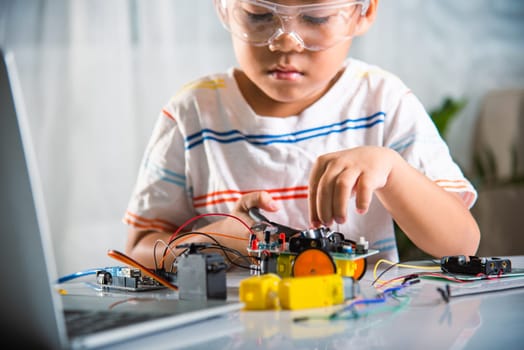 Little child tighten the nut with a screwdriver to assemble car toy, Asian kid boy assembling the Arduino robot car homework project at home, education AI technology workshop school learning lesson