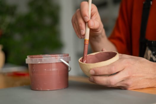 Close-up of a potter's hands with a brush painting ceramic dishes
