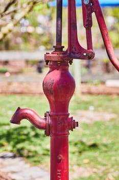 Vintage red water pump in Fort Wayne, bathed in sunlight amid green foliage, symbolizing enduring history.