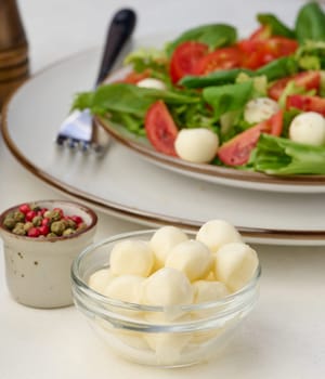 Mozzarella balls in glass bowl and salad on a white background, close up