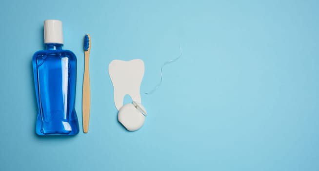 Plastic bottle with mouthwash, wooden toothbrush on blue background, top view