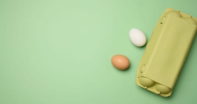 Chicken egg and paper storage box on green background, top view. Copy space