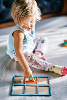 Little girl sitting on the bed and touching a puzzle with her finger. High quality photo