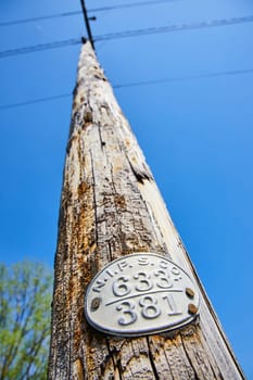 Aged utility pole with a weathered ID plate under a clear sky in Warsaw, Indiana, symbolizing enduring service.