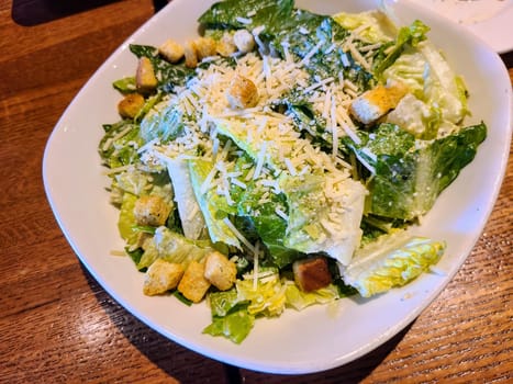 Fresh Caesar salad in a white dish on a wooden table, epitomizing gourmet dining in Fort Wayne, Indiana.