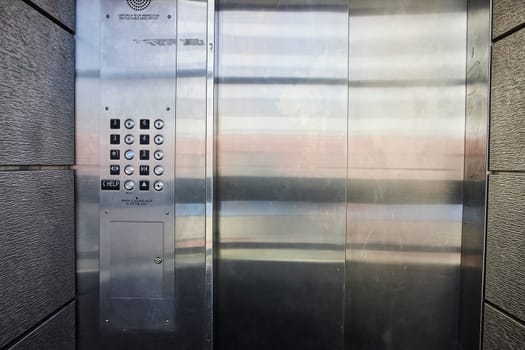 Modern elevator panel with safety features and sleek steel doors, ideal for urban architectural themes.