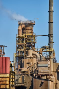 Industrial plant in Warsaw, Indiana, with smokestack and rusted machinery under clear blue skies.