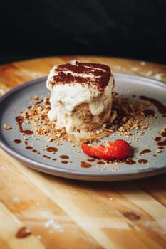 Delectable TiramiTiramisu dessert topped with cocoa powder alongside crushed biscuits and strawberry garnish on a wooden table.su Served on a Ceramic Plate Garnished With Strawberry and Cocoa. High quality photo