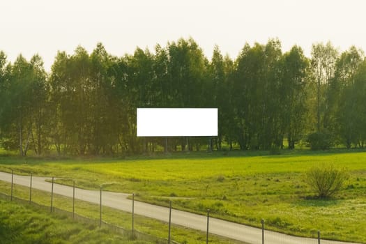 A field with a road cutting through it, surrounded by trees in the distance.