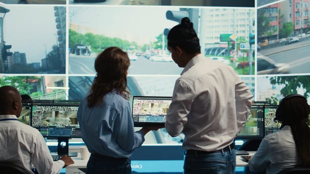 Diverse team following city traffic on a display in monitoring room, reviewing CCTV satellite radar footage. Employees working on surveillance and data collecting, control center. Camera B.