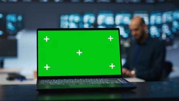 Focus on green screen laptop in server room used by man in blurry background to safeguard data from threats. Close up shot of chroma key notebook used by specialist protecting supercomputers