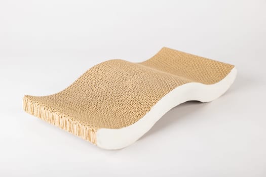 A white background highlights a modern abstract cat scratching post and lounge bed made with corrugated cardboard. cat alertness and playful paw showcase its love for this essential feline furniture.