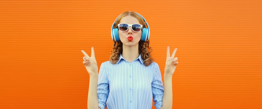 Happy modern happy young woman listening to music with headphones on bright colorful orange background