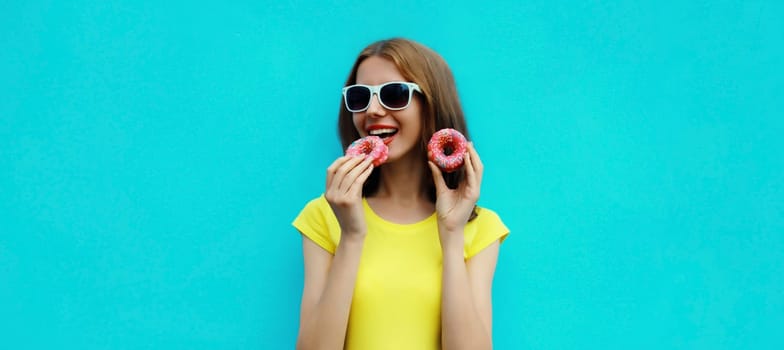 Portrait of happy cheerful smiling young woman with sweet donut having fun on blue background