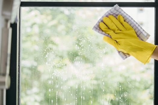 With happiness a young woman maid sprays and wipes office windows. Her housework routine emphasizes purity hygiene and transparent cleanliness for sparkling windows.