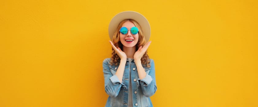 Portrait of stylish happy surprised young woman wearing summer straw hat, glasses posing on orange background
