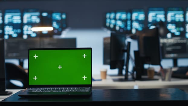 Focus on isolated screen laptop in data center with man in blurry background coding, managing server rows. Close up shot of chroma key notebook and IT expert overseeing rackmounts operating data
