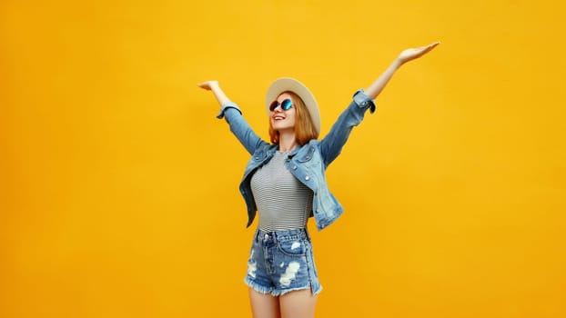 Summer holidays, inspired happy cheerful smiling young woman raising her hands up wearing denim clothing, straw hat on colorful yellow background