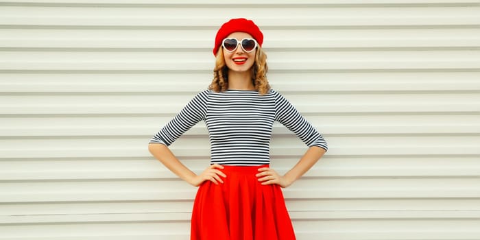 Portrait of beautiful happy smiling young woman model posing in red skirt, french beret, heart shaped sunglasses on white background