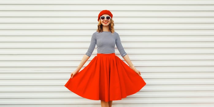 Portrait of beautiful happy smiling young woman model posing in red skirt, french beret, heart shaped sunglasses on white background