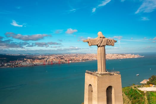 Aerial View of Christ the King Statue overlooking Tagus River and cityscape under blue sky. Bird's eye view Catholic monument and city. Lisbon, Portugal