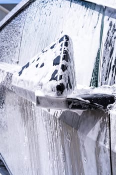 Denver, Colorado, USA-May 5, 2024-This image captures a close-up view of the Tesla Cybertruck side mirror covered in soap suds during a car wash, emphasizing the vehicle unique angular design and rugged exterior.