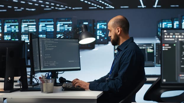 IT engineer programming in server hub housing advanced equipment storing massive datasets. Technician typing code on computer to mend data center racks doing complex computational operations