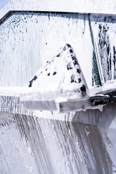 Denver, Colorado, USA-May 5, 2024-This image captures a close-up view of the Tesla Cybertruck side mirror covered in soap suds during a car wash, emphasizing the vehicle unique angular design and rugged exterior.