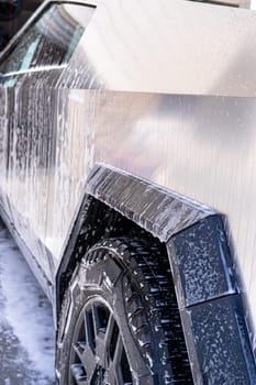 Denver, Colorado, USA-May 5, 2024-This image features a close-up view of the Tesla Cybertruck wheel and angular body design covered in soap and water during a thorough car wash, highlighting the unique textures and robust details of the electric truck.