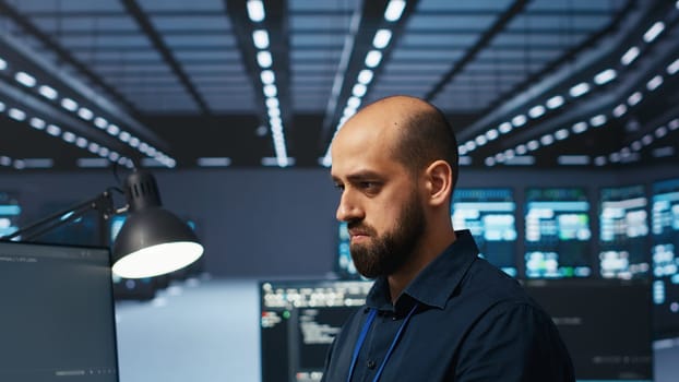 Programmer writing code, working in network security data center facility, ensuring optimal performance. IT specialist using PC to monitor energy consumption across operational server racks