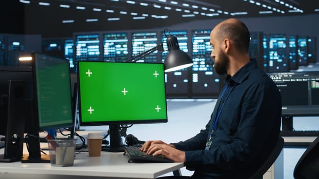 Man typing code on green screen computer in high tech data center with server rows providing computing resources. IT specialist using mockup PC to oversee rackmounts operating data