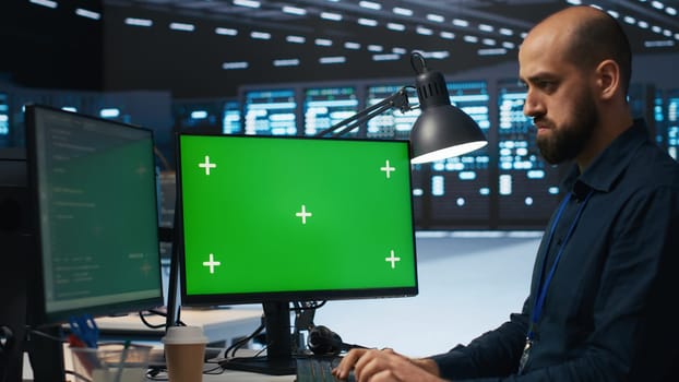 System administrator working on green screen computers in data center, ensuring optimal performance. Worker monitoring energy consumption across servers with mockup PC displays